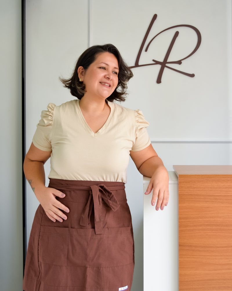 Lis Rodrigues no ateliê, em frente ao logo LR